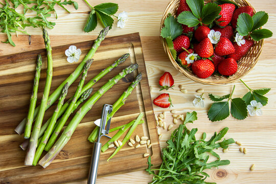 fresh vegetables on wooden background, fresh strawberries   and green asparagus, peel the asparagus, flower the strawberries, cooking, ingredients 