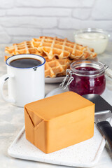 Piece of Norwegian brown cheese with waffles, lingon jam and cup of coffee,  vertical