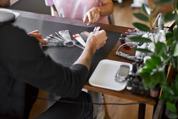 Male confident manicure master in salon with beautiful female light hair woman client