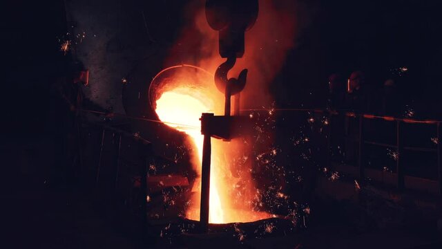 Blast furnace foundry metallurgical factory with liquid iron pouring to container, cast process. Steel mill iron smelting process with bright sparks and smoke.