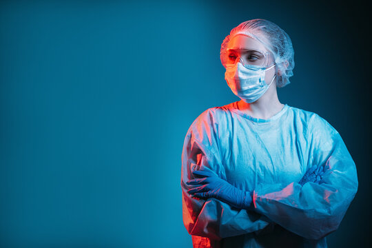 Covid-19 Outbreak. Pandemic Banner. Respiratory Infection Risk. Portrait Of Disturbed Pensive Female Doctor In Ppe Face Mask Goggles Looking At Copy Space Isolated On Dark Blue Background.