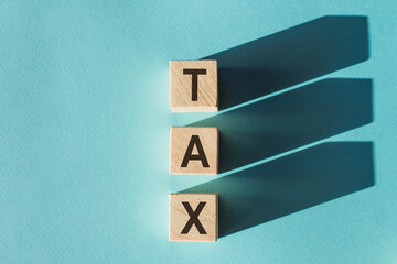 Wooden cubes building word TAX on light blue background.