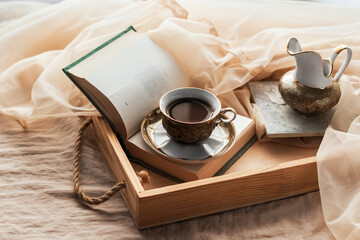 Morning coffee. A cup of coffee on a wooden tray and an open book on a silk bed. Cozy home interior, lifestyle, romantic atmosphere.