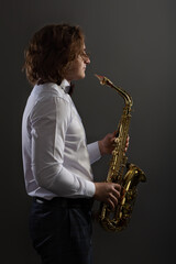 Fototapeta na wymiar Studio portrait of young cool man with saxophone on dark background.