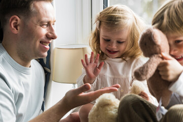 Children sit on the windowsill. Happy dad playing with children. Gives five. A boy and a girl are playing.