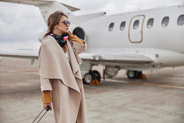 Mature business woman in coat near her jet in airport - obrazy, fototapety, plakaty