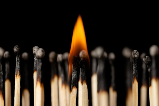 Couple of burnt matches standing next to each other, holding a small fire above them. A lot of burned safety matches around symbolizing society.