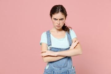 Young frowning serious angry caucasian woman wear trendy denim clothes blue t-shirt look camera hold hands crossed folded isolated on pastel pink background studio portrait. People lifestyle concept.