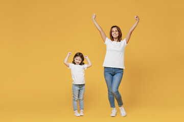 Full length happy woman in basic white t-shirt have fun with cute child baby girl 5-6 years old hold hands. Mom little kid daughter isolated on yellow color background studio Mother's Day love family