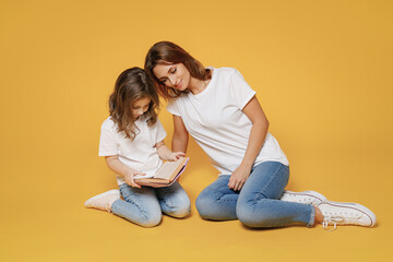 Obraz na płótnie Canvas Full body length happy woman in basic white tshirt sit on floor read book child baby girl 5-6 years old Mom mum little kid daughter isolated on yellow color background studio Mother's Day love family
