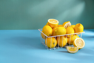 Bright ripe yellow lemons in white basket on light green solid color background with copy space, the concept of spring lack of vitamins and healthy lifestyle.
