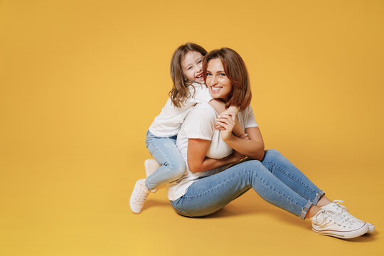 Full body length happy woman in basic white t-shirt have fun sit on floor child baby girl 5-6 years old Mom mum little kid daughter isolated on yellow color background studio Mother's Day love family.