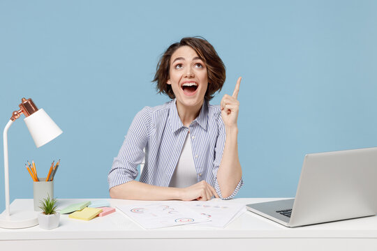 Young Excited Successful Employee Business Woman In Casual Shirt Sit Work At White Office Desk With Pc Laptop Point Index Finger Overhead On Copy Space Area Mock Up Isolated On Blue Background Studio.