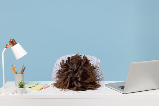 Young tired exhausted frustrated secretary employee business woman wearing casual shirt sit work sleep laid her head down on white office desk with pc laptop isolated on pastel blue background studio.
