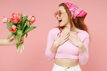 Man hand hold give bouquet of tulips flowers. Young surprised woman 20s in rose clothes bandana glasses hold folded arms isolated on pastel pink color background studio portrait Spring season concept