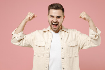Fototapeta na wymiar Young expressive caucasian fun man in jacket white t-shirt showing biceps muscles on hand demonstrating strength power isolated on pastel pink color background studio portrait People lifestyle concept