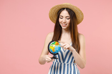 Young geography student tourist fun woman in summer clothes striped dress straw hat holding in hands Earth world globe spin touch choose country isolated on pastel pink background studio portrait