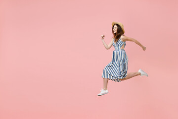 Full length side view young sporty fun smiling happy overjoyed caucasian woman in summer clothes striped dress straw hat jump high run fast hurrying up isolated on pastel pink color background studio.