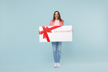 Full length young fun happy excited overjoyed woman wearing pastel pink clothes glasses hold large huge gift voucher flyer mock up isolated on blue color background studio People lifestyle concept - obrazy, fototapety, plakaty