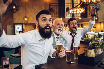 Three businessmen cheering while watching football match in a cafe bar.