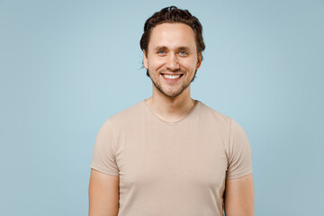 Obraz premium Young smiling happy positive friendly cheerful caucasian attractive man 20s wear casual basic beige t-shirt looking camera isolated on pastel blue background studio portrait. People lifestyle concept.