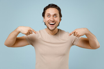 Young shocked happy amazed surprised impressed attractive man wear casual basic beige t-shirt point index finger on himself isolated on pastel blue background studio portrait People lifestyle concept