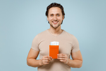 Traveler smiling happy tourist man 20s in casual basic t-shirt hold passport tickets isolated on yellow orange background. Passenger traveling abroad on weekends getaway. Air flight journey concept