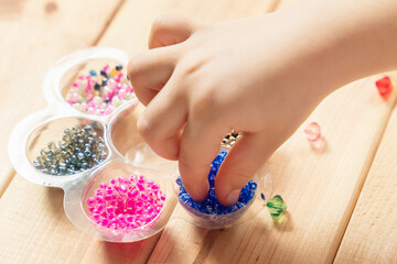 The child makes jewelry with his own hands, stringing colorful beads on a thread