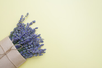 Top view of a bouquet of lavender in a craft bag on a yellow background with copy space. Spring or summer concept