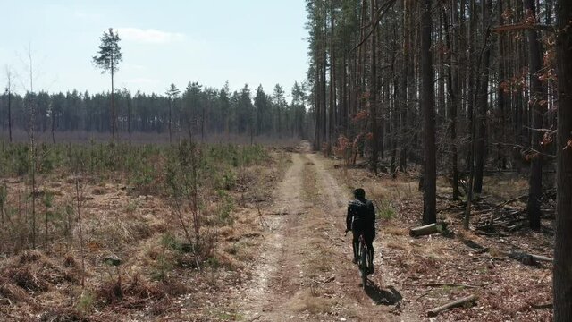 Professional cyclist riding on gravel bike on a bumpy dirt road in the forest.