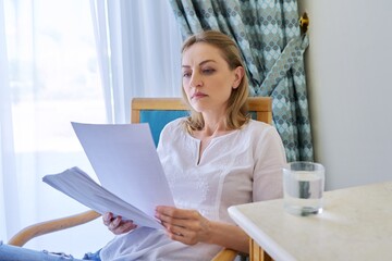 Obraz premium Sad emotion on face of mature woman reading paper letter, contract, document.