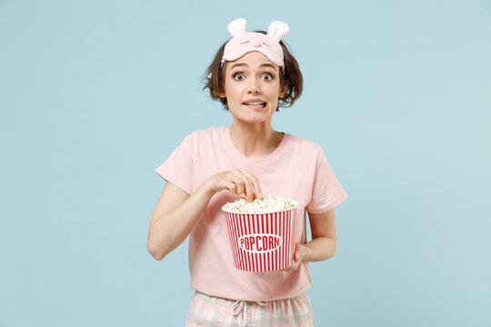 Young Shocked Scared Woman In Pajamas Jam Sleep Eye Mask Rest Relaxing At Home Hold Takeaway Bucket With Pop Corn Eat Snack Isolated On Pastel Blue Background Studio. Good Mood Night Bedtime Concept.