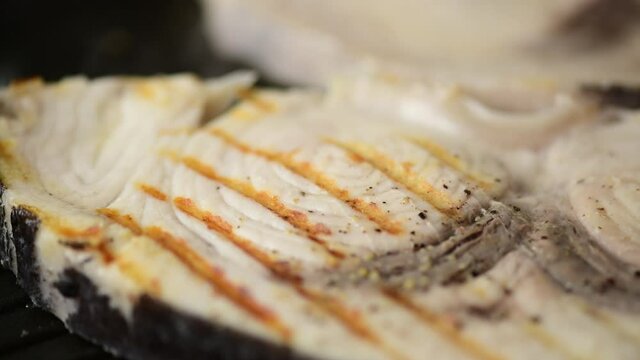 Swordfish Xiphais gladius steak portion cooking on a grill pan with smoke and steam, close up, zoom in