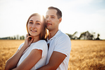 Portrait of a happy boy and girl on the background of a ripe field with wheat. A loving couple hugging on a sunny day. Man and woman in the summer in a wheat field.