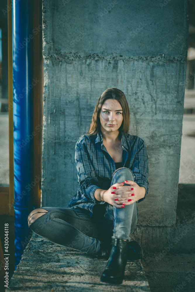 Poster full body shot of a beautiful woman wearing a checkered green shirt sitting on stone during sunset