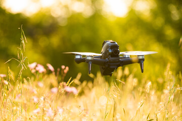 Stunning view of an FPV drone flying over a grass field during a beautiful sunset. Concept of recreational pursuits, hobby.