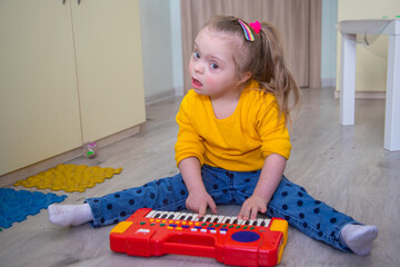 Down syndrome in a little girl, a child, a child playing a toy piano, early development of disabled...