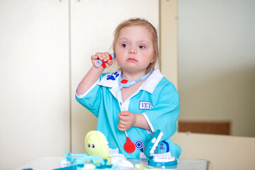 Down syndrome in a little girl, a child in a doctor's costume playing with a doll and with medical...