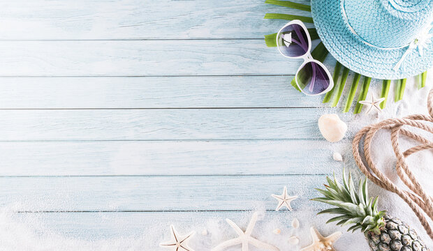 Summer holiday, travel and vacation concept. Beach hat with sunglasses, starfish, rope, pineapple and sea shell on pastel blue wooden background.