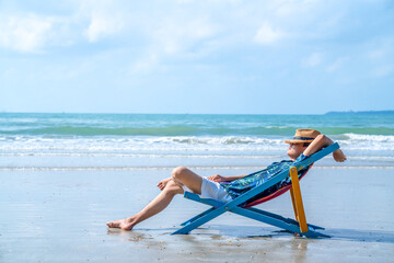 Asian man resting on beach chair at tropical beach. Happy guy sunbathing or nap on sunbed by the...
