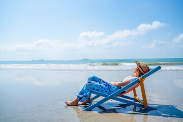 Young Asian woman resting on beach chair at tropical beach. Happy girl sunbathing on sunbed by the...