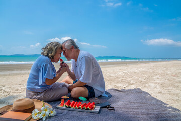 Happy Asian family on beach vacation. Senior couple sitting on blanket have picnic together on sea beach. Healthy elderly husband and wife relax and enjoy outdoor lifestyle activity on summer vacation - Powered by Adobe