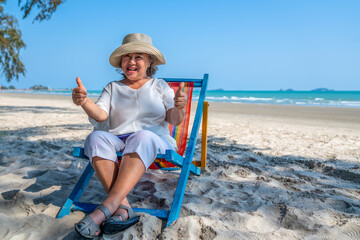 Healthy Asian senior woman resting on sunbed by the sea. Retirement elderly female sitting on beach...