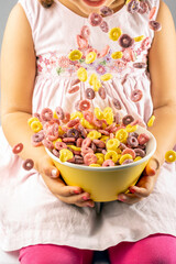 colored cereal rings falling into a yellow bowl held by a girl