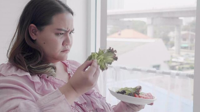 Young asian woman fat dislike vegetable salad, female hate vegetable but eating for dieting weight loss, healthy food, female expression and emotion, plus size, nutrition and detox for health.