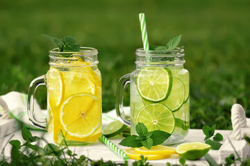 Cold refreshing homemade lemonade with mint, lemon and lime in mason jars on a summer lawn