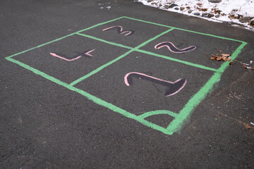 A leisure and creative childhood game of four squares. The squares are outlined using green caulk and the numbers are black and pink in color. The outdoor children's game is on black asphalt. 