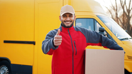 Smiling delivery man showing thumb up and looking at camera. High quality photo