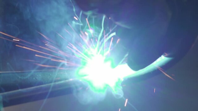 Abstract close up image of welding two metal pipes, with bright green flame and pink red sparks flying in all directions