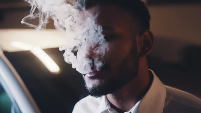 Smoking, nicotine addiction, social issues concept. Adult mixed race relaxed man exhaling cloud of cigarette smoke. High quality 4k footage